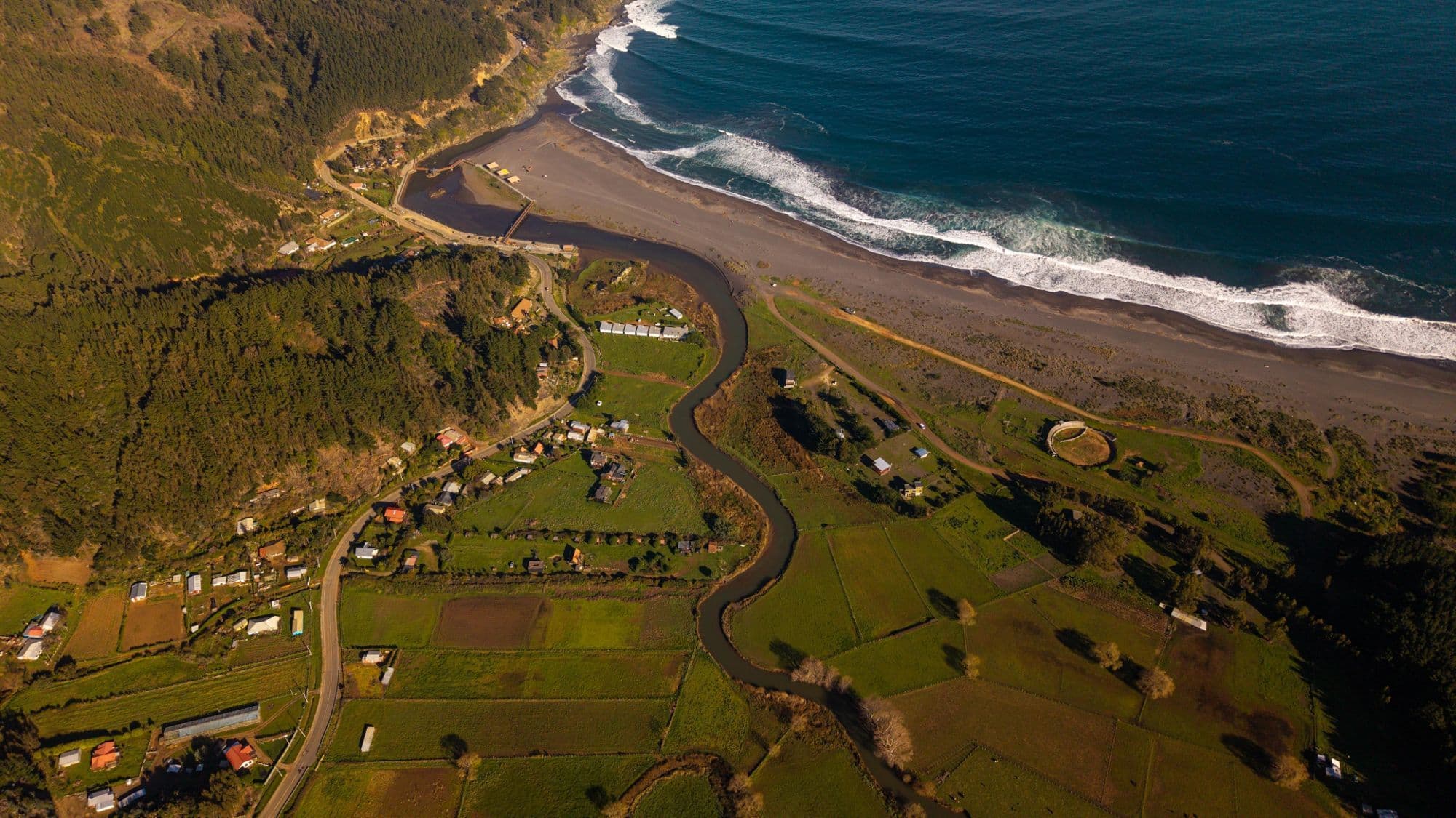 Vista aérea de Buchupureo: el río serpentea entre potreros hasta desembocar en la playa, con el camping Queltehues a su orilla