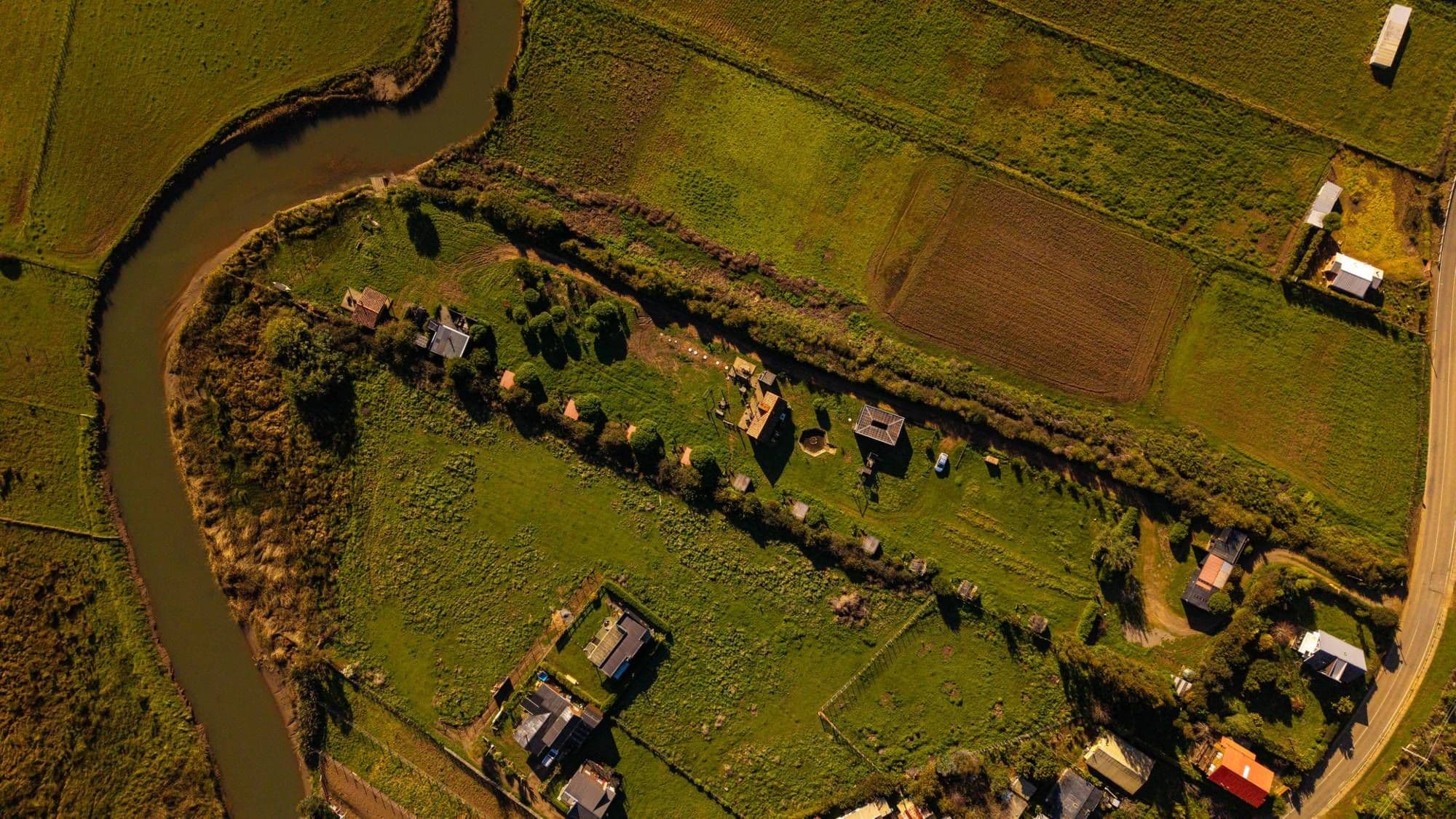 Vista cenital del camping Queltehues: los quinchos en diagonal, el Club House al centro y el estero a un costado